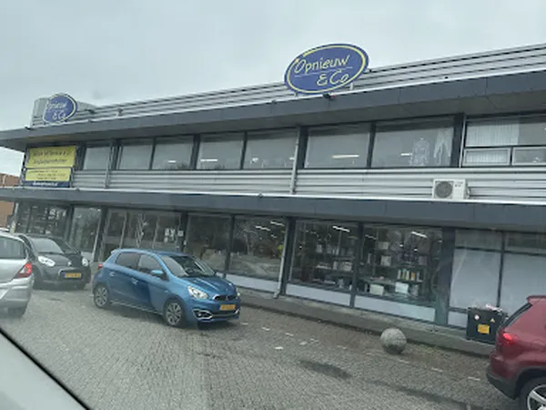 Gevel van kringloopwinkel Opnieuw & Co met blauwe auto geparkeerd ervoor