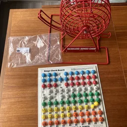 Bingo-spel met rode kooi, bingo-bordkaart en witte plastic balletjes in zakje