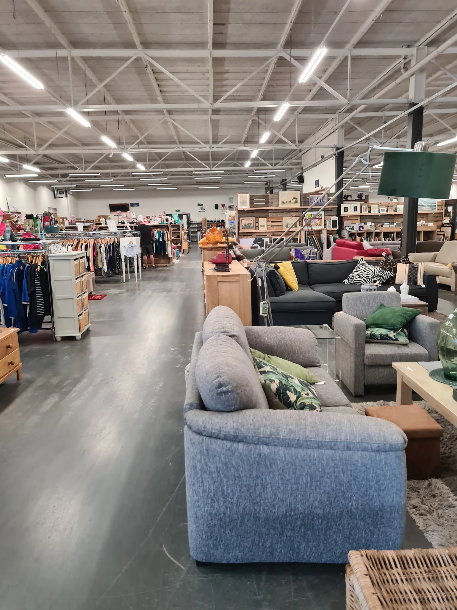 Overzicht van kringloopwinkel met meubels, kleding en huishoudspullen op de vloer