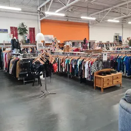 Winkelvloer met kledingrekken vol tweedehands kleding, houten meubel op voorgrond, oranje muur op achtergrond
