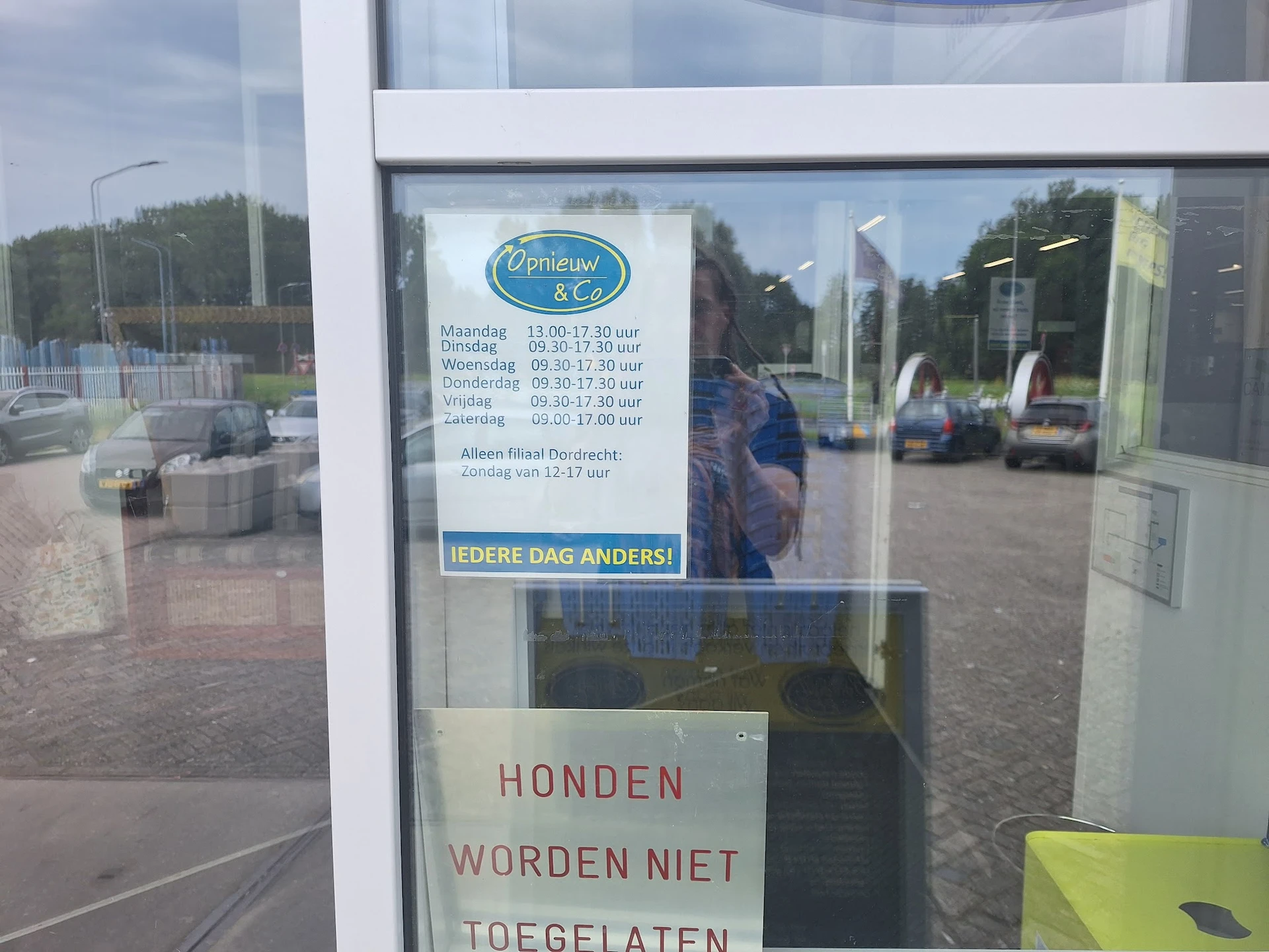 Glazen deur van kringloopwinkel met openingstijden en tekstbord over honden
