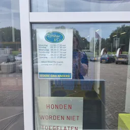 Glazen deur van kringloopwinkel met openingstijden en tekstbord over honden