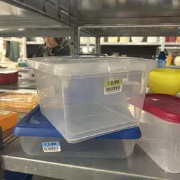 Doorzichtige plastic opbergbakken met blauwe en rode deksels, uitgestald in een kringloopwinkel met prijskaartjes