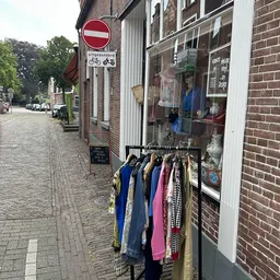 Rek met kleding buiten aan de gevel van de winkel, met jassen en vesten in verschillende kleuren
