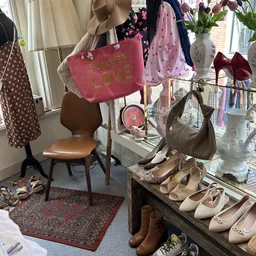 Vintage tassen, schoenen en accessoires uitgestald in de winkel, waaronder een roze tas met 'LOVE' opschrift