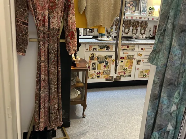 Winkelvloer met vintage kleding aan hangers, houten meubel en winkelkasten met artikelen in achtergrond