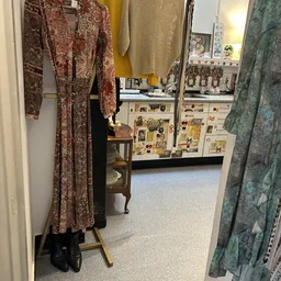 Winkelvloer met vintage kleding aan hangers, houten meubel en winkelkasten met artikelen in achtergrond