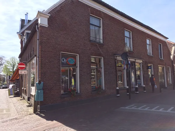 Baksteinen gevel van kringloopwinkel met etalages en ramen aan een straathoek
