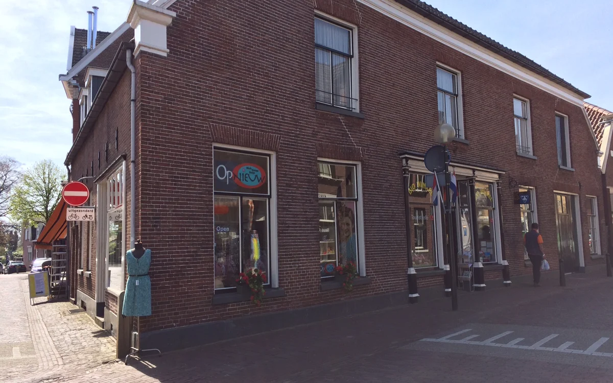 Baksteinen gevel van kringloopwinkel met etalages en ramen aan een straathoek