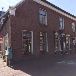 Baksteinen gevel van kringloopwinkel met etalages en ramen aan een straathoek