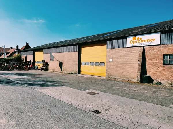 Gevel van kringloopwinkel Oprommer met gele laaddeuren en logo op bakstenen pand