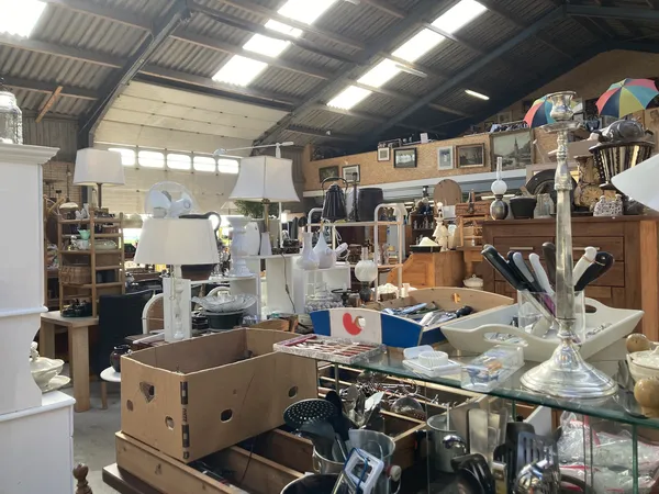 Overzicht van de kringloopwinkel met diverse meubels, huishoudartikelen en spullen op tafels en stellingen