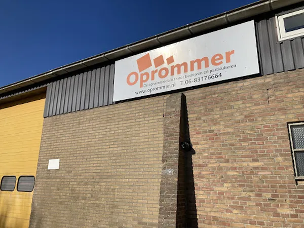 Gevel van kringloopwinkel Oprommerloads met oranje logo op witte panelen en bakstenen muur