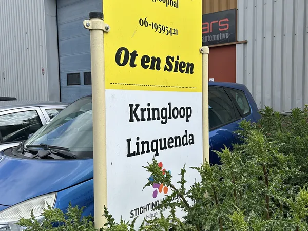 Geel bord met 'Ot en Sien' en 'Kringloop Linguenda' zichtbaar buiten de winkel, geparkeerde auto's en industriële gebouwen op