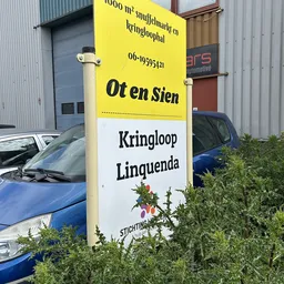 Geel bord met 'Ot en Sien' en 'Kringloop Linguenda' zichtbaar buiten de winkel, geparkeerde auto's en industriële gebouwen op