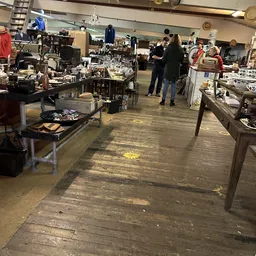 Binnenzicht van kringloopwinkel met tafels, stellingen en diverse spullen langs de wanden