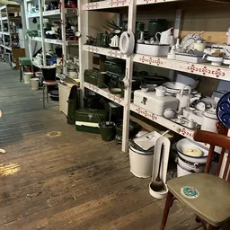 Stellingen vol met huishoudelijke artikelen: pannen, schalen, keukengereedschap en serviesgoed in een kringloopwinkel