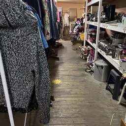 Winkelgang met kledingrekken links en stellingen met huishoudartikelen rechts