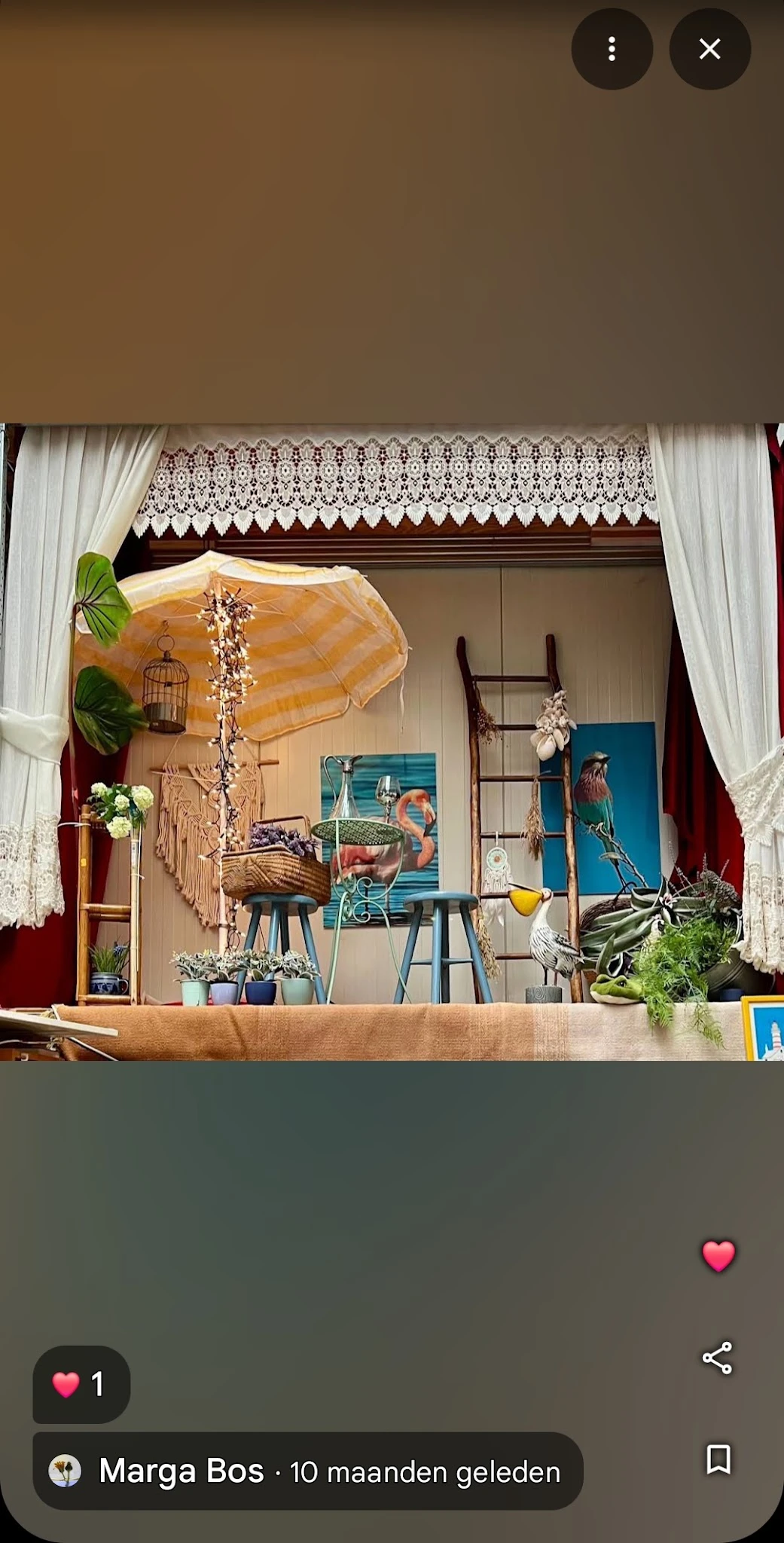 Etalage met vintage en tweedehands spullen: parasol, vogels, schilderijen, plantjes en decoratieve objecten