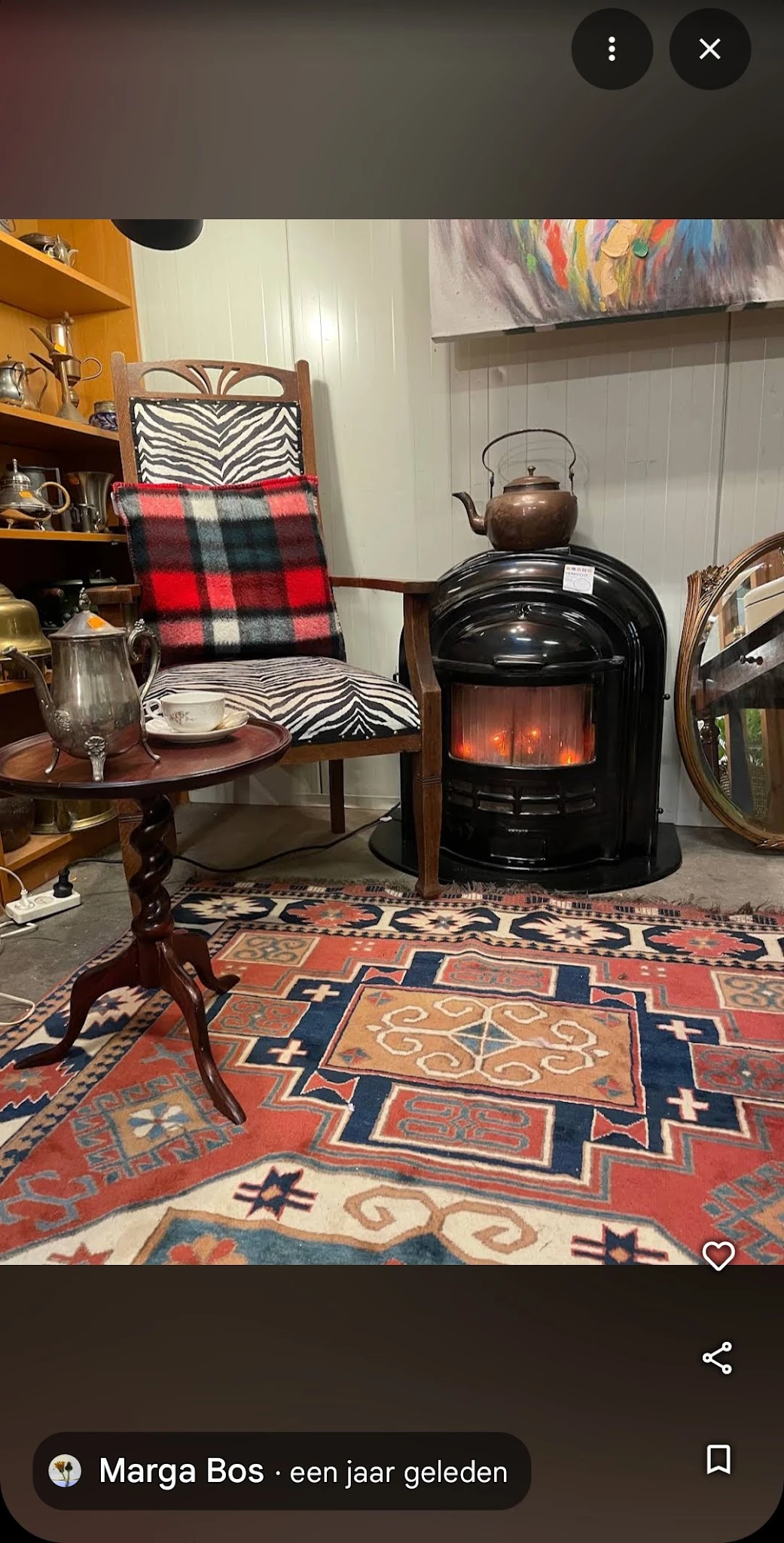 Tweedehands interieurstukken: houten tafel, rood-zwart geruit kussen, zwarte elektrische kachel, ornamentaal tapijt en spiege