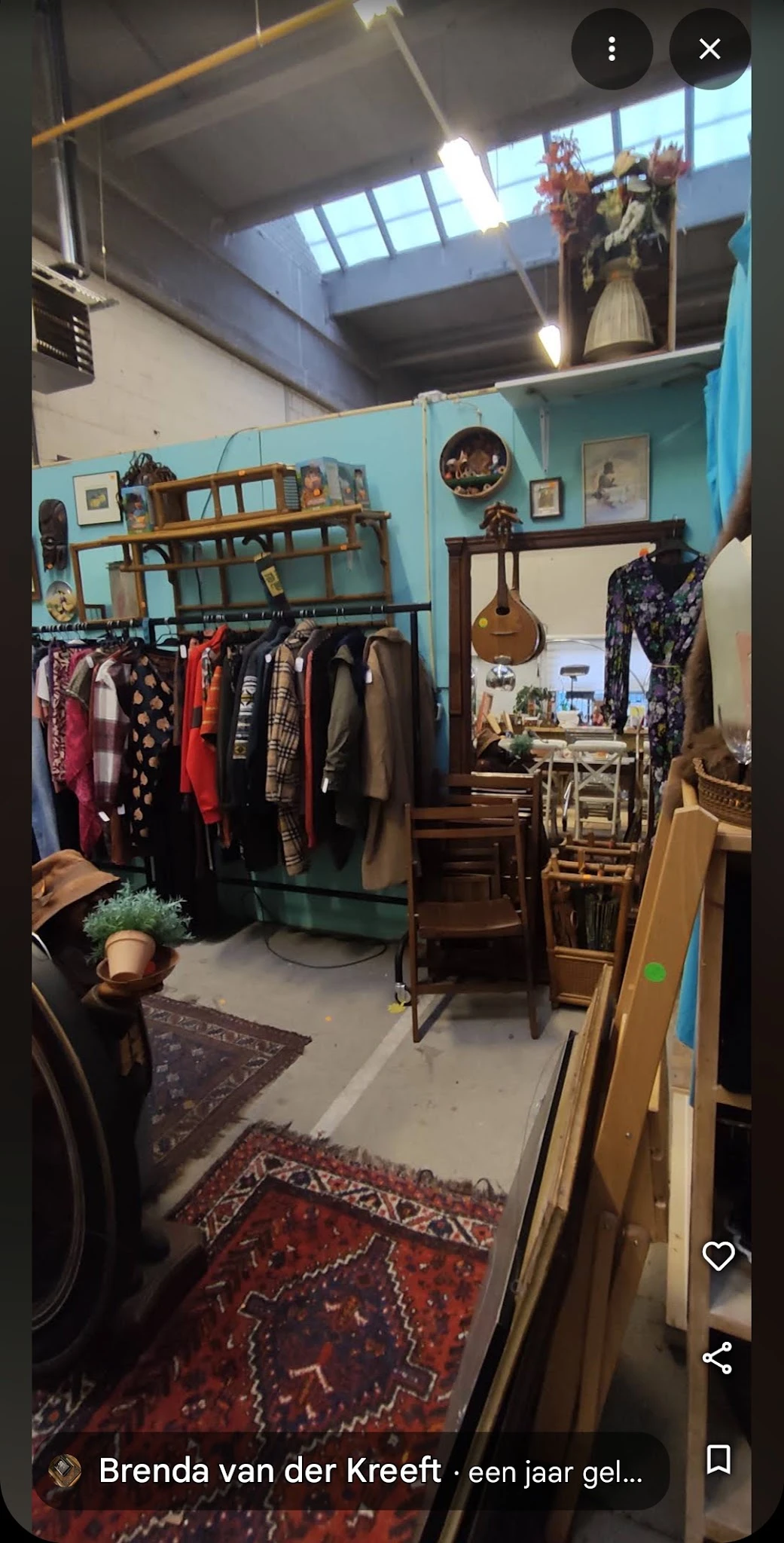 Winkelinterieur met kledingrek, houten meubels, spiegel en diverse spullen tegen turquoise muur