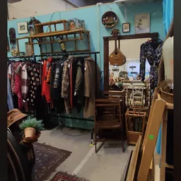 Winkelinterieur met kledingrek, houten meubels, spiegel en diverse spullen tegen turquoise muur