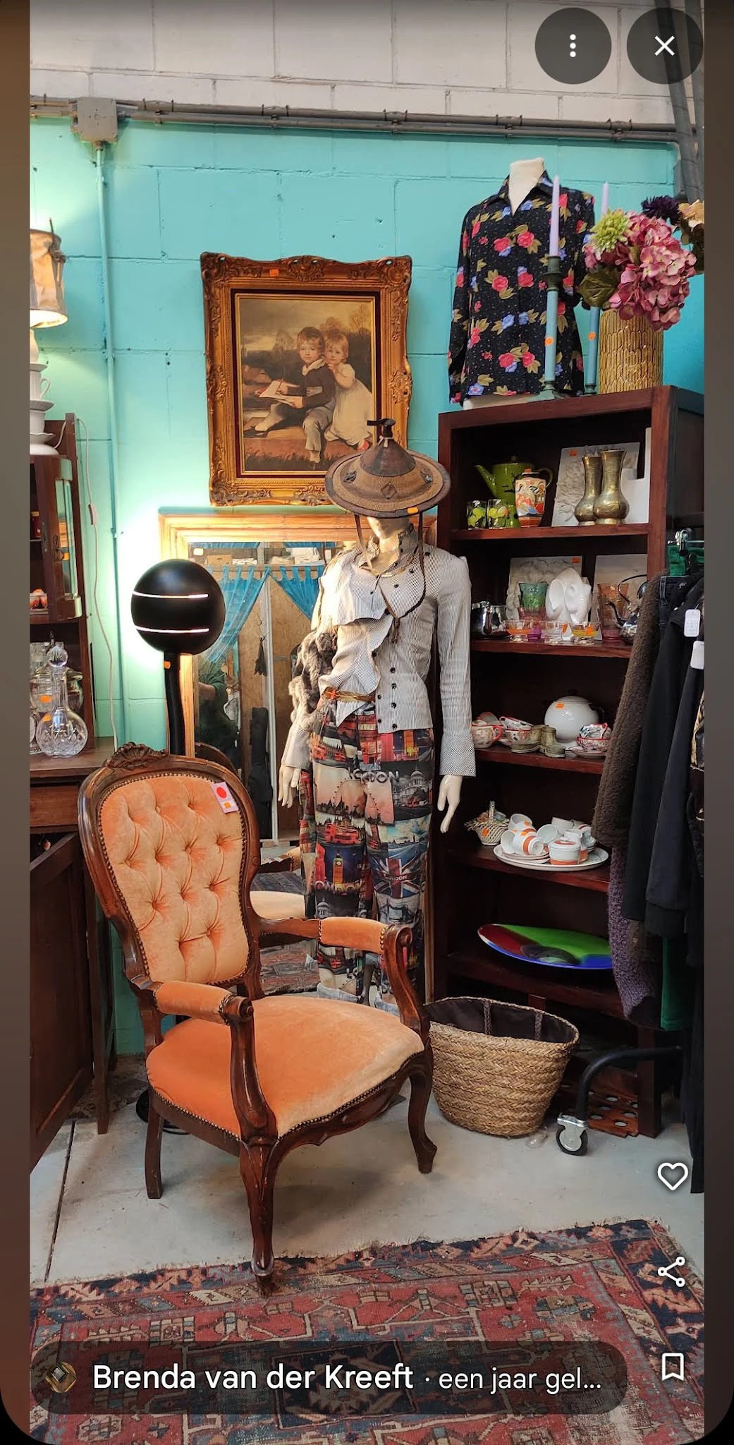 Etalage met vintage kledingrekken, een buste met kleding, decoratieve objecten en porselein op houten planken
