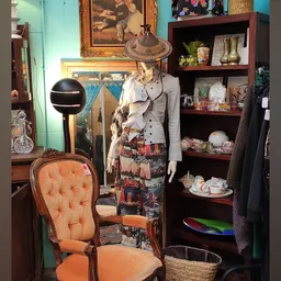 Etalage met vintage kledingrekken, een buste met kleding, decoratieve objecten en porselein op houten planken