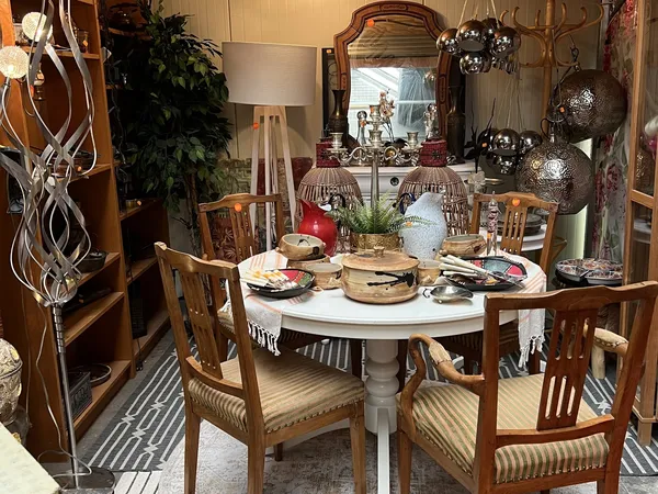 Ingerichte eethoek met ronde witte tafel, houten stoelen, servies en decoraties in een kringloopwinkel
