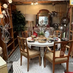 Ingerichte eethoek met ronde tafel, houten stoelen en decoratieve objecten in een kringloopwinkel