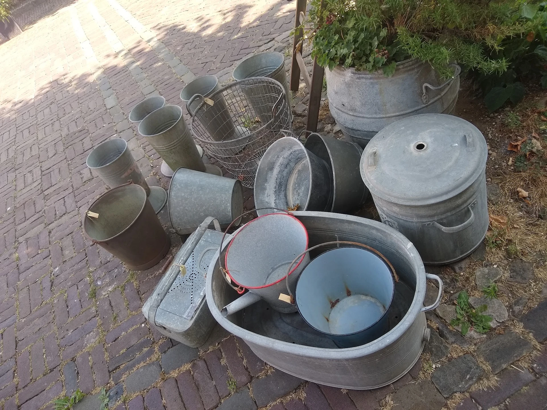Verzameling gebruikte huishoudelijke items zoals metalen emmers, potten en bakken op een terras