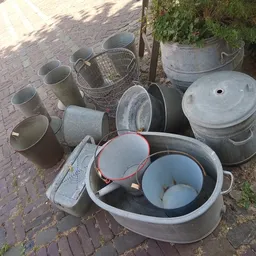 Verzameling gebruikte huishoudelijke items zoals metalen emmers, potten en bakken op een terras