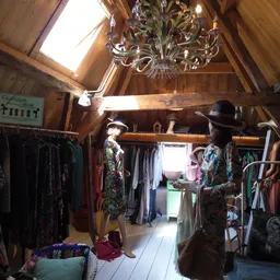 Interieur van kringloopwinkel met houten balken, rekken met kleding, mannequins met outfits en kroonluchter