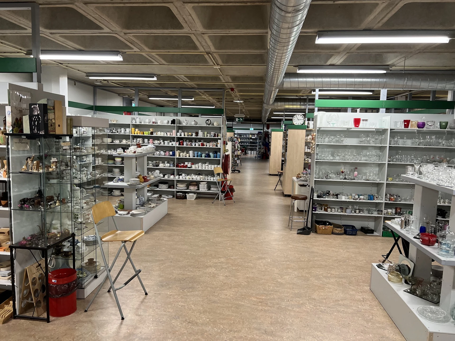 Ruime winkelvloer met stellingen vol spullen, tl-verlichting, hoge plafonds met balken in kringloopwinkel