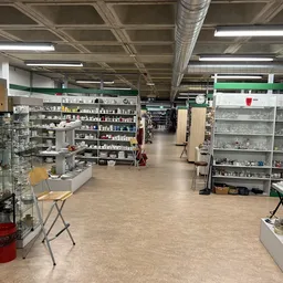 Ruime winkelvloer met stellingen vol spullen, tl-verlichting, hoge plafonds met balken in kringloopwinkel