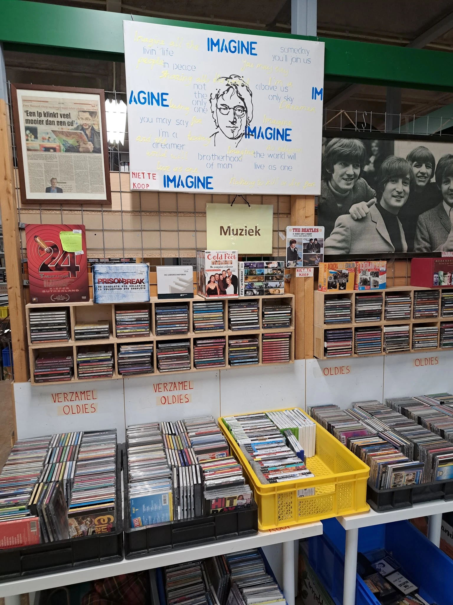 Rekken en dozen met cd's, muziekalben en verzamelitems in een kringloopwinkel, met bordenkasten met cd's en vintage posters a
