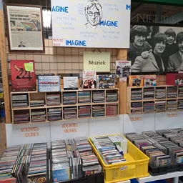 Rekken en dozen met cd's, muziekalben en verzamelitems in een kringloopwinkel, met bordenkasten met cd's en vintage posters a