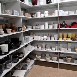 Stellingen met wit serviesgoed, bekers, potten en ander huishoudelijk artikel in een kringloopwinkel