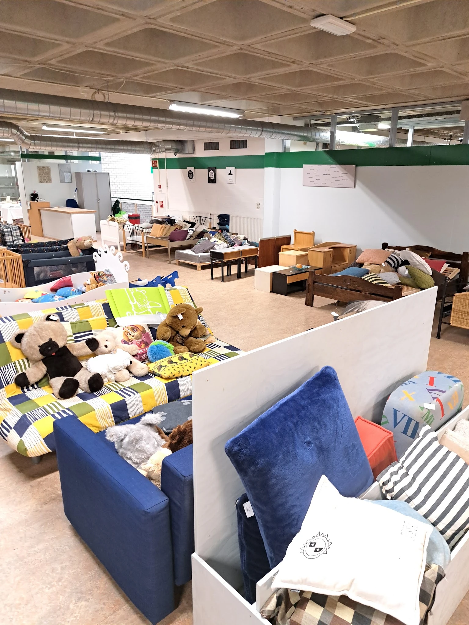 Ruim interieur van kringloopwinkel met diverse meubels, bedden, dozen en huishoudelijke artikelen uitgestald