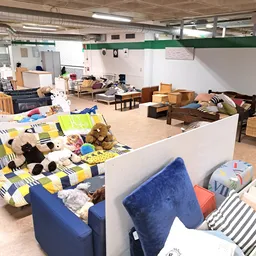 Ruim interieur van kringloopwinkel met diverse meubels, bedden, dozen en huishoudelijke artikelen uitgestald