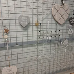 Uitgestalde sieraden en decoratieve items opgehangen aan een grijs gaas displaypaneel in de winkel