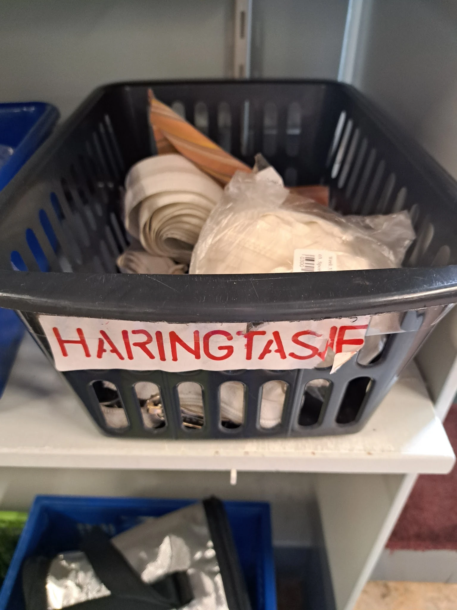 Zwarte plastic mand met wit serviesgoed en huishoudartikelen, gelabeld met rode tekst