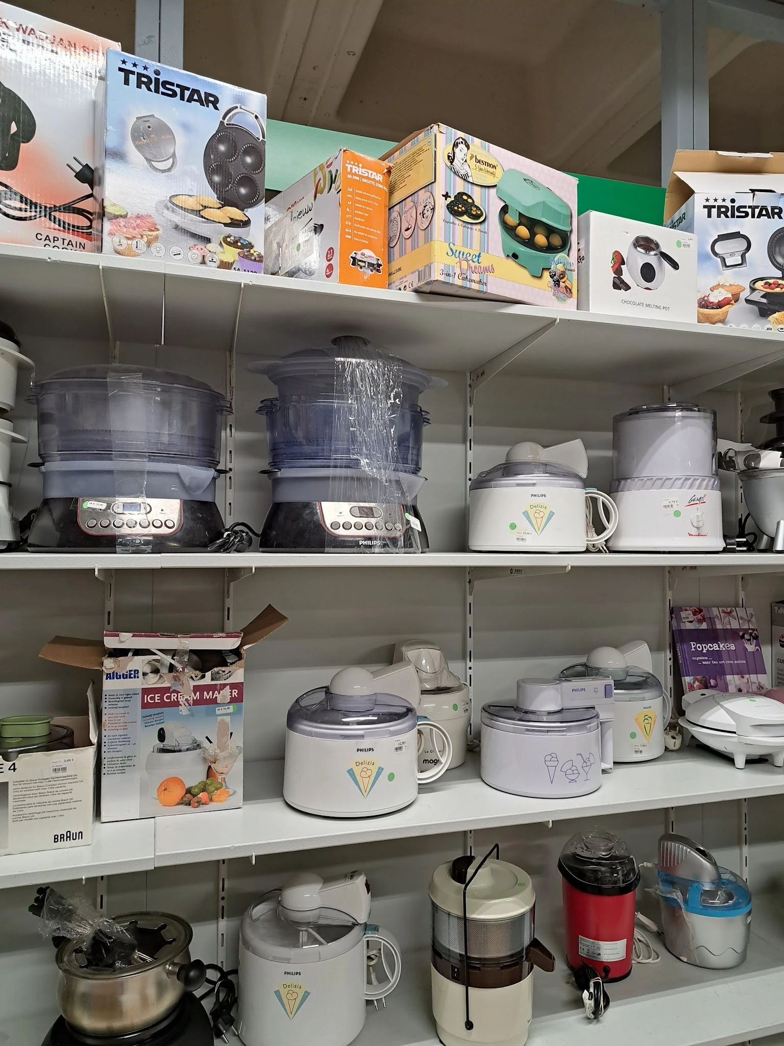 Kastplanken met tweedehands keukenaccessoires zoals rijstkokers, stoomers en waterkokers