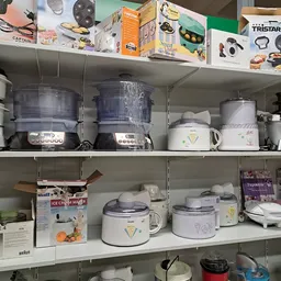 Kastplanken met tweedehands keukenaccessoires zoals rijstkokers, stoomers en waterkokers