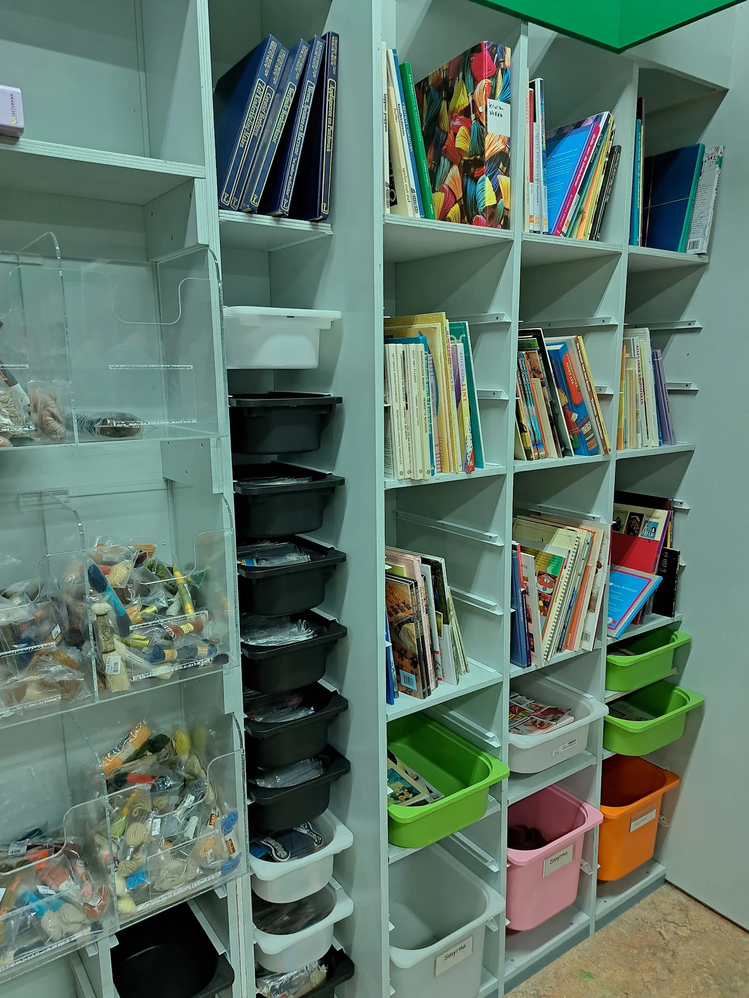 Witte stellingen met boeken, zwarte opbergboxen en groene bakken in kringloopwinkel