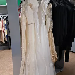 Rekken met tweedehands bruids- en feestkleding in crème en ivoor tinten