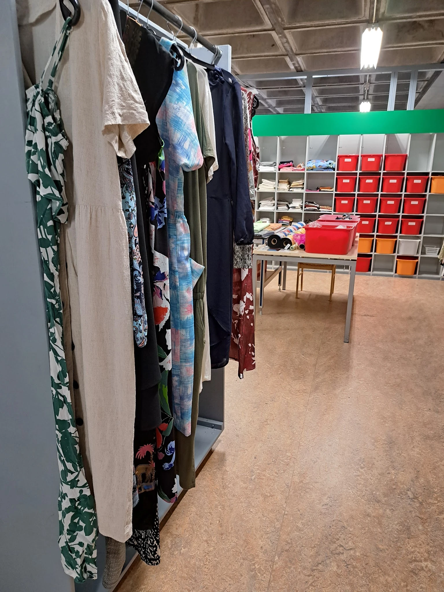 Winkelinterieur met kledingrek links en rode opbergboxen op planken rechts, tafel in het midden