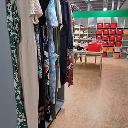 Winkelinterieur met kledingrek links en rode opbergboxen op planken rechts, tafel in het midden