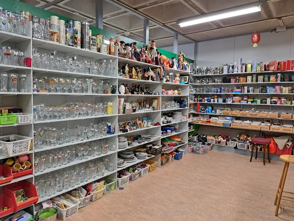 Winkelbinnenruimte met uitgebreide stellingen vol glazen potten, servies en huishoudartikelen, houten vloer en rode bakken in