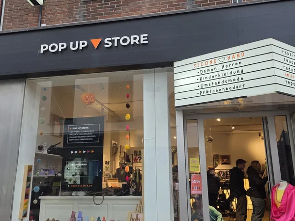 Gevel van Pop Up Store met zwart winkelfront, grote glazen ramen met uitgestalde kleding en een bordje 'Secondhand' aan de zi